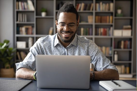 man sitting at desk working on his laptop while smiling